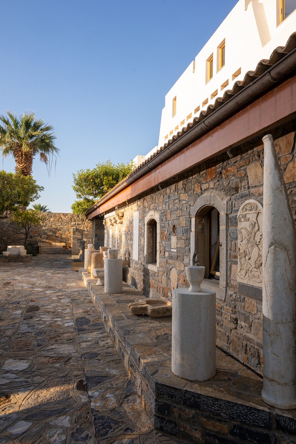 Architectural detail of the entry-courtyard wall at Elounda Mare: ancient marble fragments and salvaged stone composed as a single continuous surface, spanning periods of Cretan history from Minoan through Ottoman.