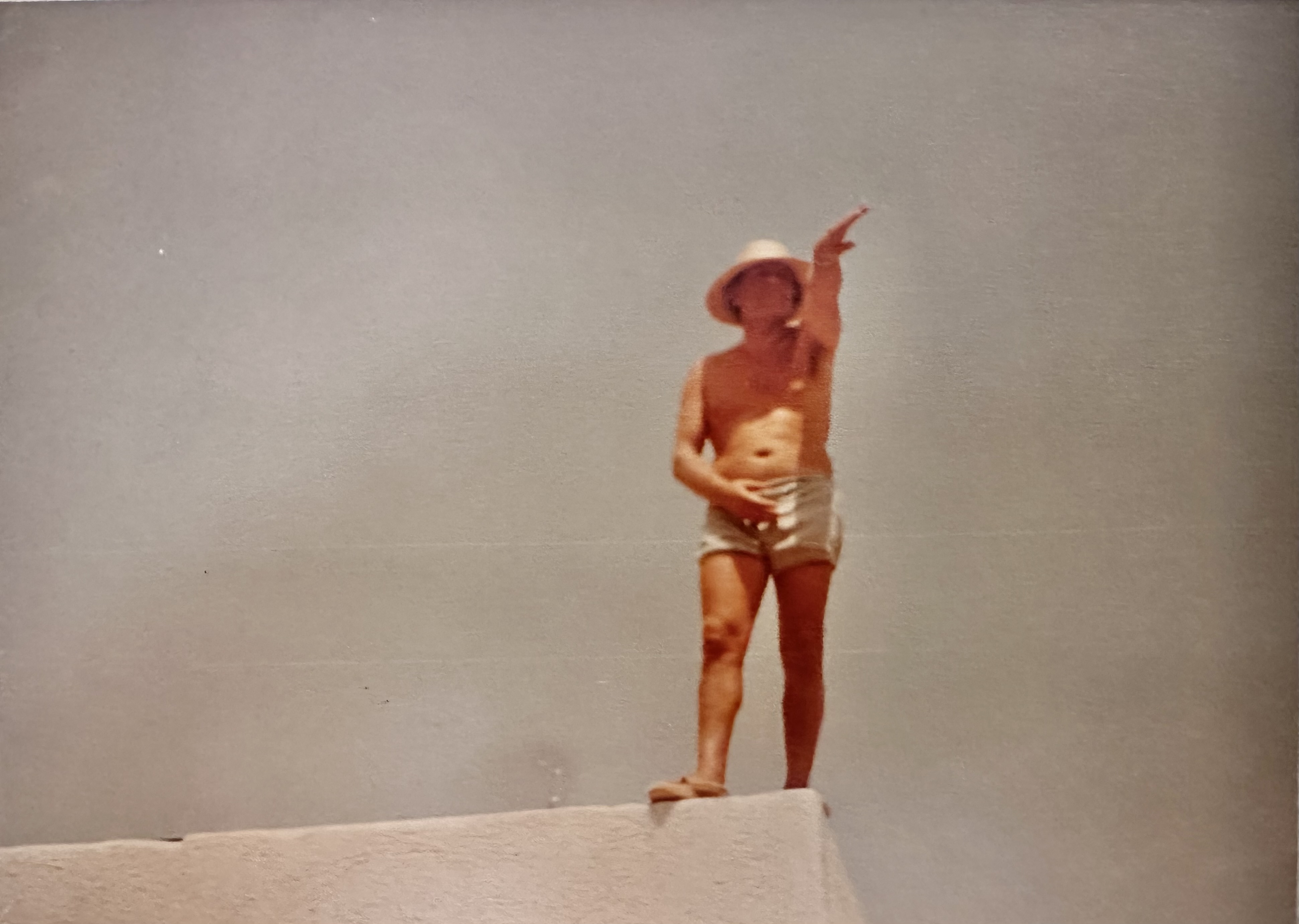 Archival photograph: Spyros Kokotos, architect, on-site at Elounda Mare in 1981, in working clothes, the gulf visible behind.