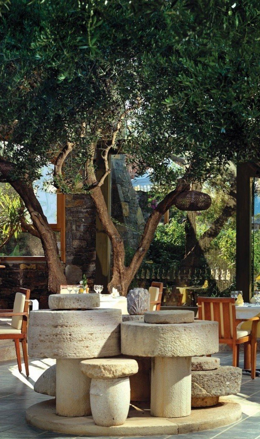 A sculptural arrangement of millstones by Spyros Kokotos, centrepiece of Elounda Peninsula's Elies restaurant — ancient grinding stones lifted from ruined olive presses across Crete, composed as a working sculpture.