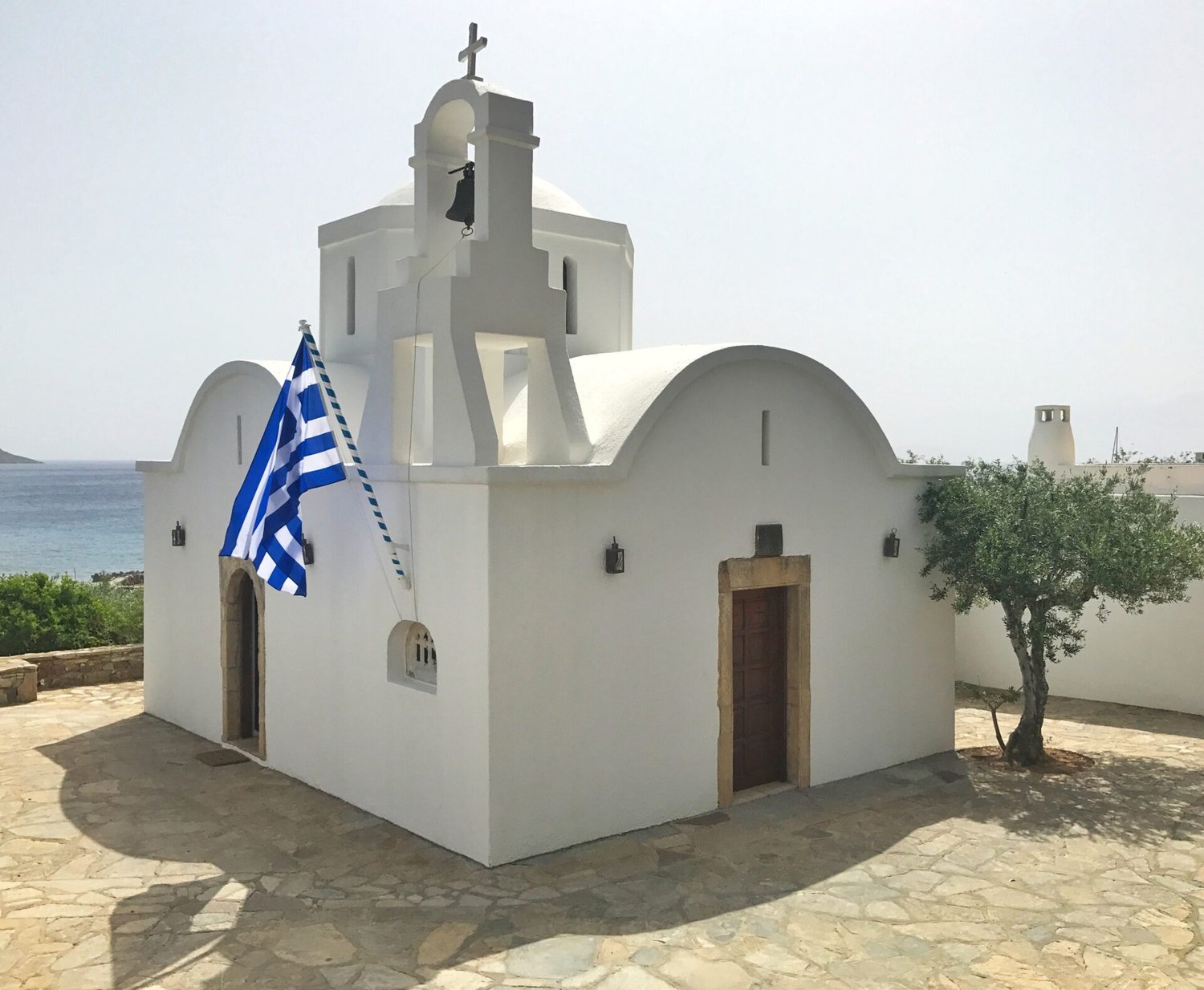 The Chapel of Santa Marina at Elounda Mare: a small working hotel chapel with iconostases from Byzantine chapels, marble fragments worked into its walls, the Greek flag flying from the bell tower.