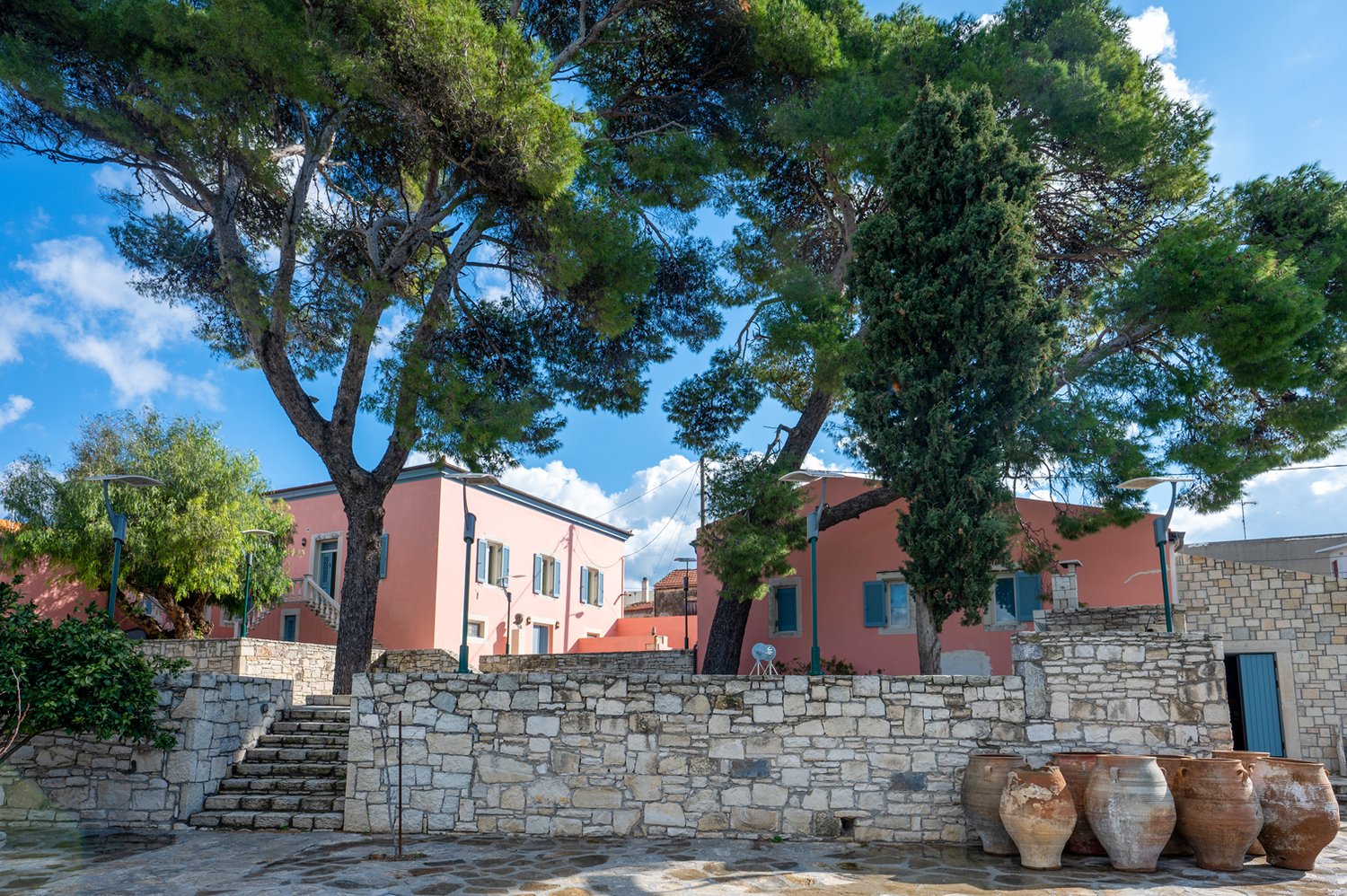 Exterior view of the Varouhas Estate in Dafnes — a low neoclassical Cretan building in pale stone, set against the cultivated vineyard slopes of the village.